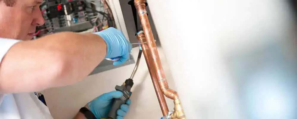 Water heater repair technician testing copper pipe connections and controls in Flagstaff, AZ
